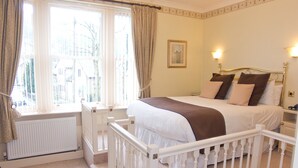 A bedroom with a bed, white curtains, a window, and a radiator. - The Old Bell Inn (Oldham)