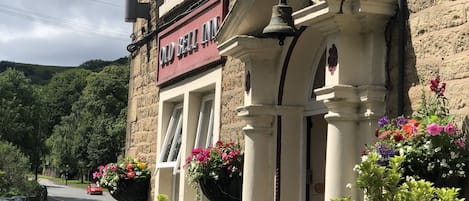 A traditional stone building with a sign reading "The Old Bell Inn Hotel." There are flower baskets on the windowsills and a bell hanging from the entrance.