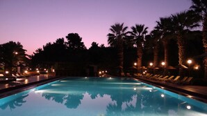 Piscina ao entardecer com espreguiçadeiras e palmeiras.