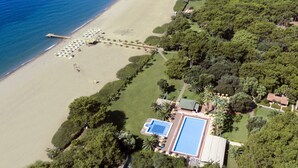 Vista aérea de um resort à beira-mar, com piscina, guarda-sóis e um píer.