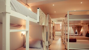 A row of bunk beds with white frames and light-colored bedding, arranged in a narrow corridor with a wooden floor. - Hello Backpacker Samui Hostel (Koh Samui)