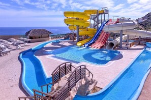 Un espace piscine doté de plusieurs toboggans et d’un bâtiment à toit de chaume.