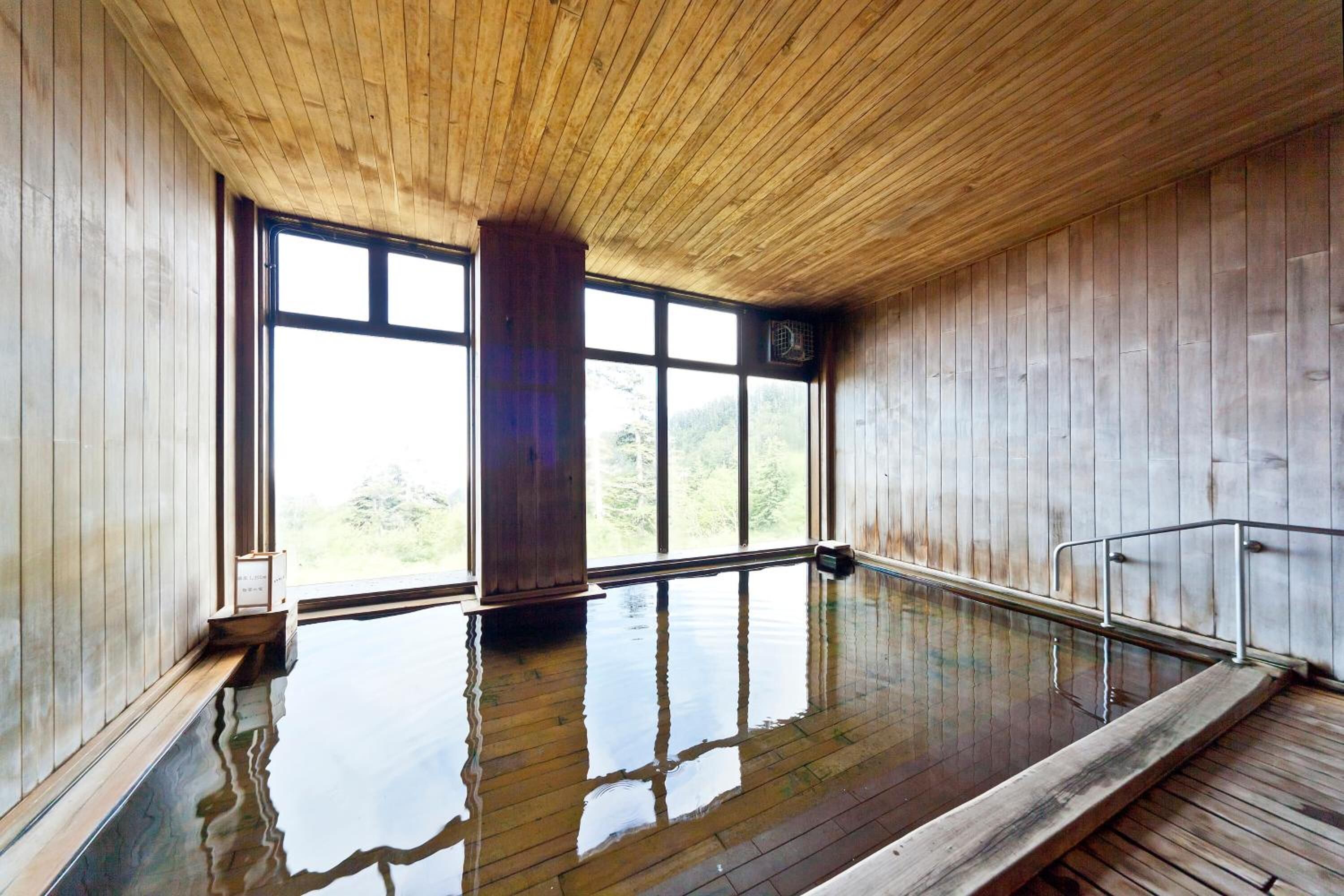 Un interior de madera con una amplia piscina cubierta, paredes de madera y grandes ventanales.