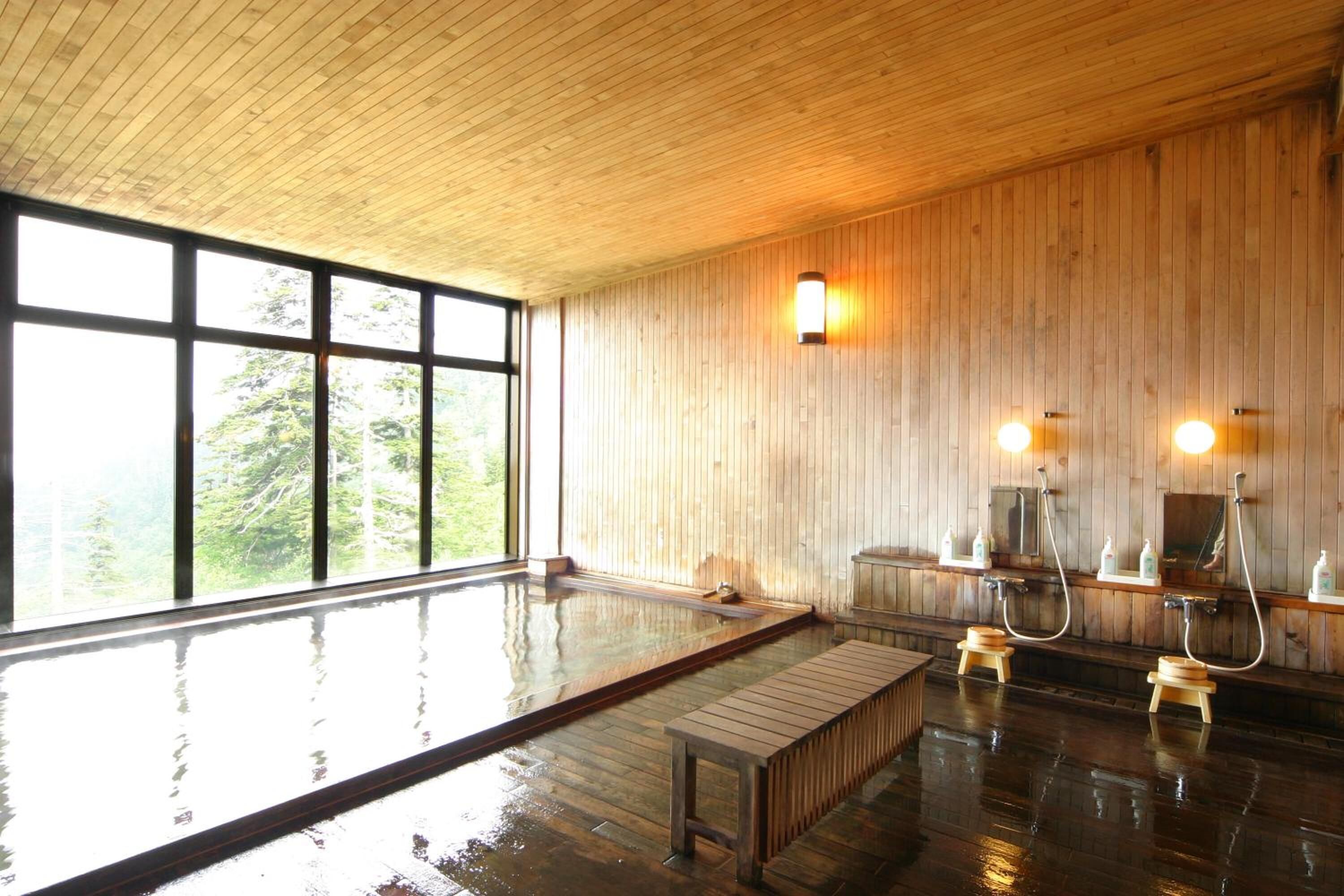 A wooden interior with a large indoor pool, wooden benches, and wall-mounted lights.