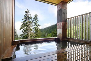 A wooden deck with a hot tub, a wooden railing, and a view of trees and mountains.