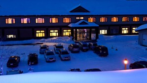 Un hotel con acceso cubierto, amplias ventanas y un estacionamiento con varios coches.