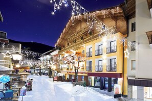 A snow-covered street with buildings, some with balconies and signage, under a starry night sky. - Fish'Inn Zell - Hotel Fischerwirt (Zell am See)