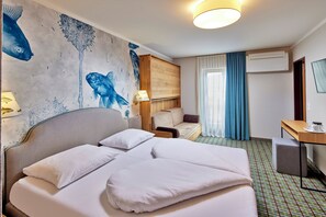 A hotel room with a bed, a desk, a chair, a sofa, and a wall mural. - Fish'Inn Zell - Hotel Fischerwirt (Zell am See)