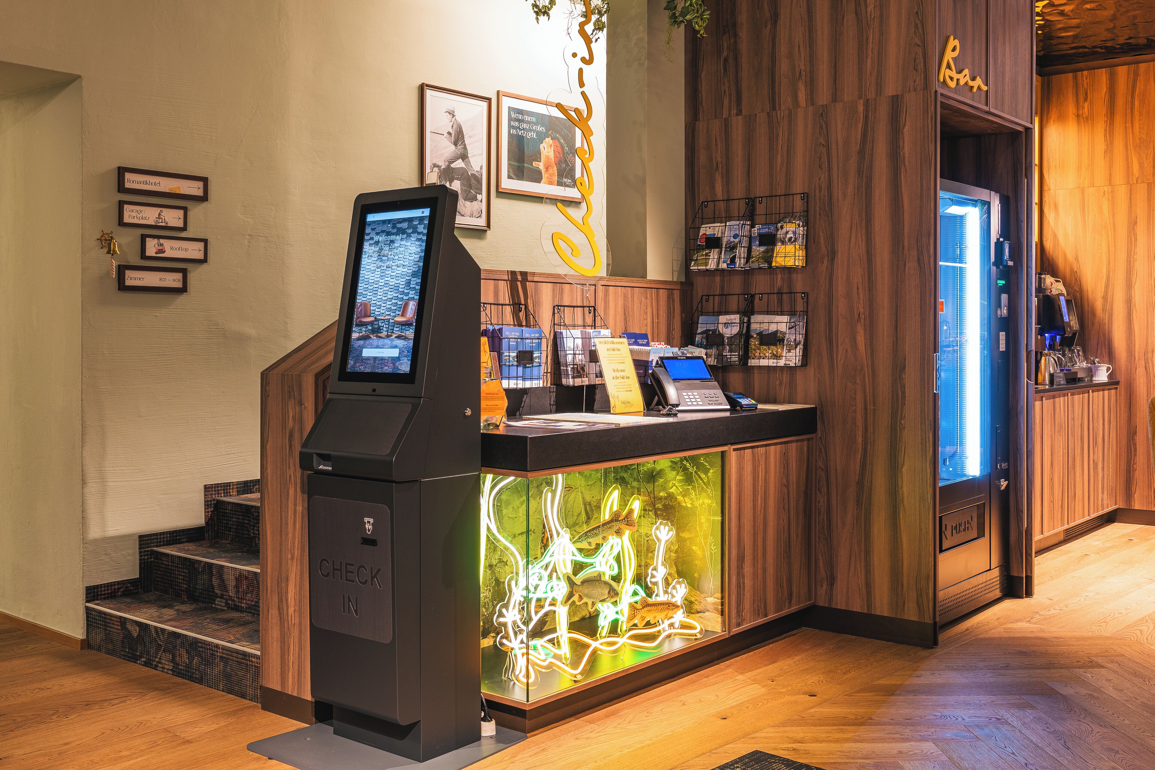 A self-service kiosk with a digital screen, a glass display case with a neon light design, and a wooden counter with a coffee machine.