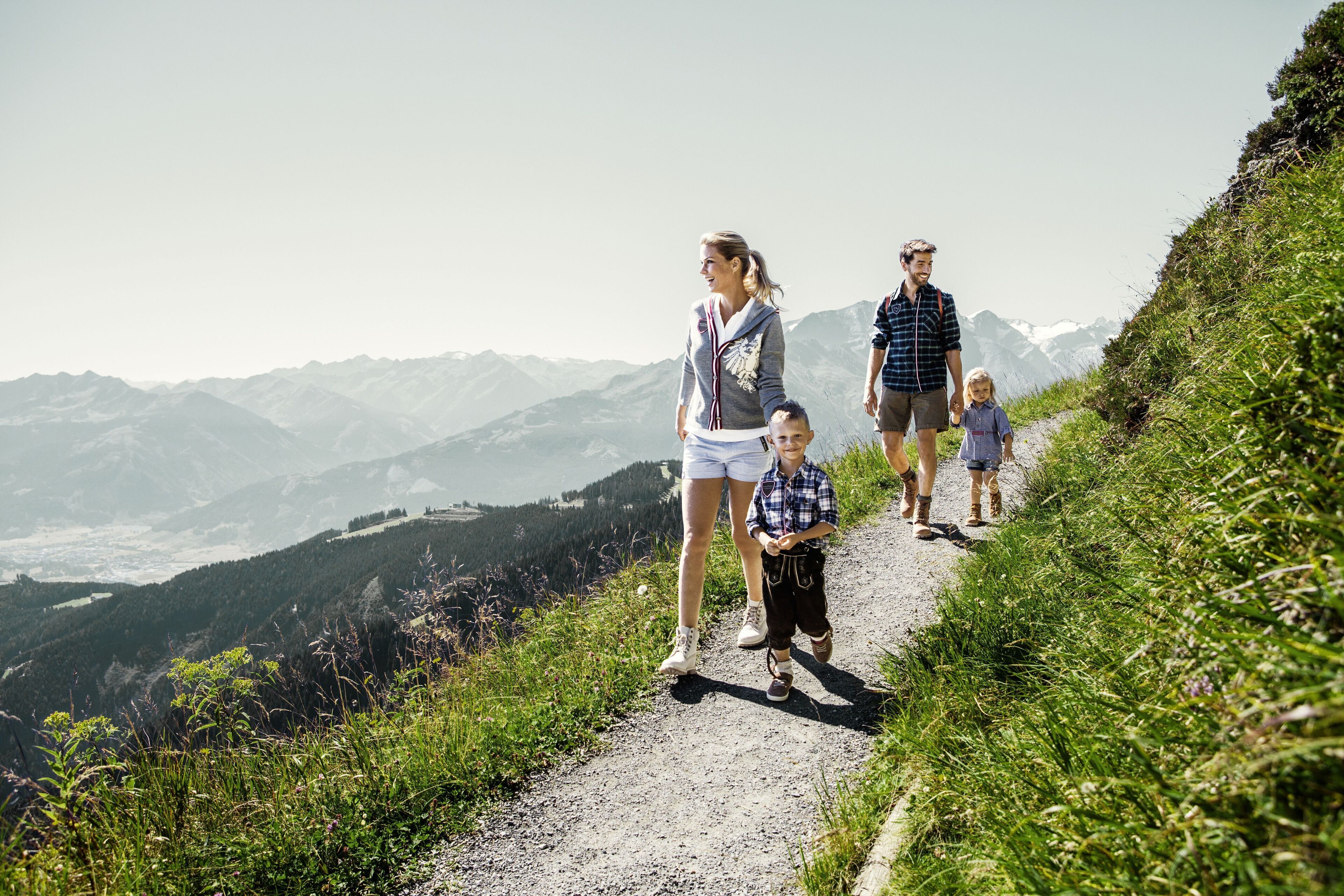 A family walking on a mountain path with a view of distant mountains.