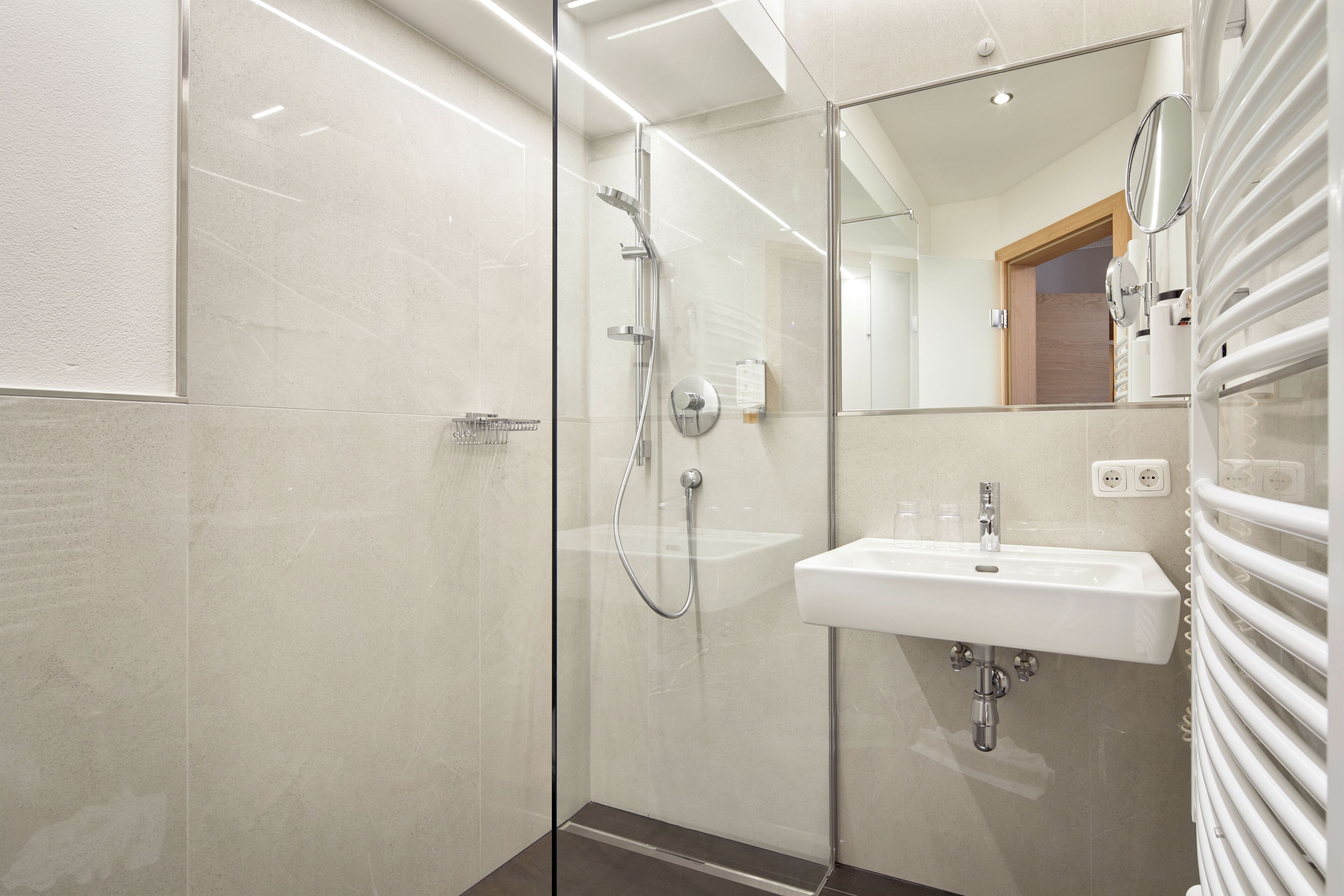 Un baño moderno con ducha envuelta en vidrio, un lavamanos blanco y un espejo.