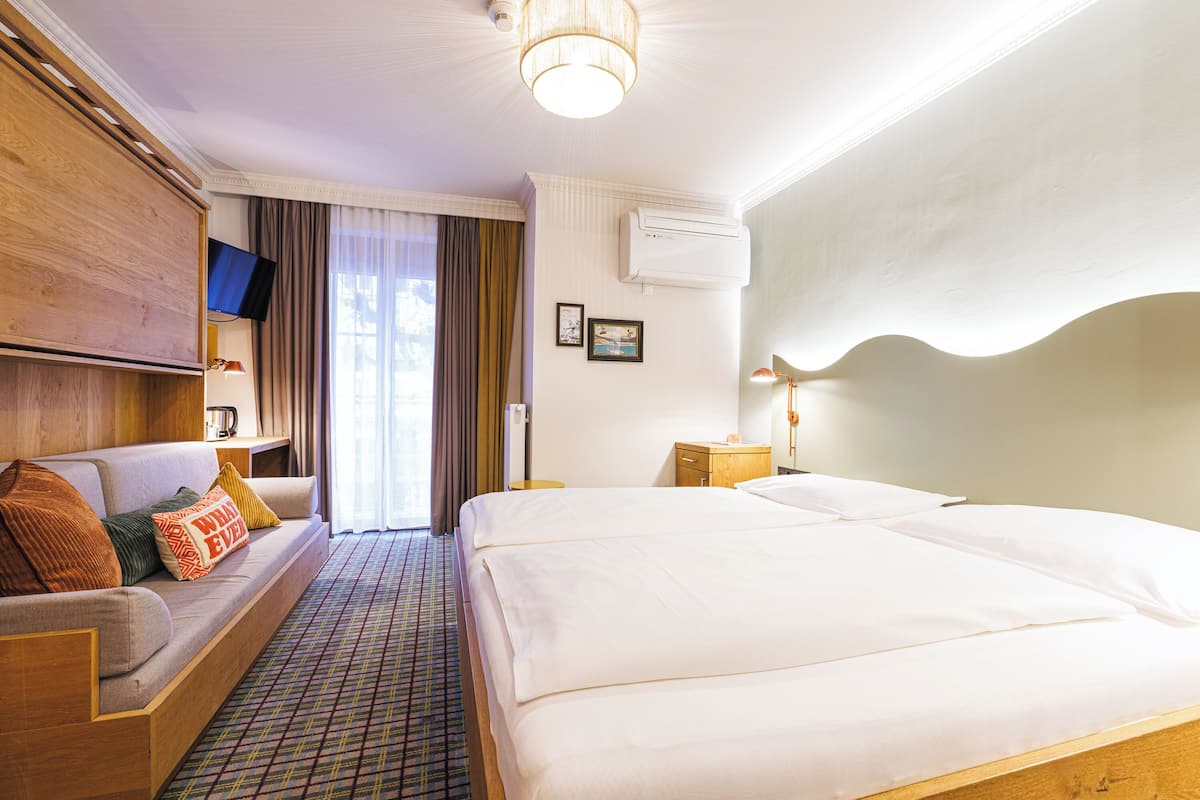 A hotel room with a sofa, two beds, a flat-screen TV, an air conditioner, and a patterned floor.