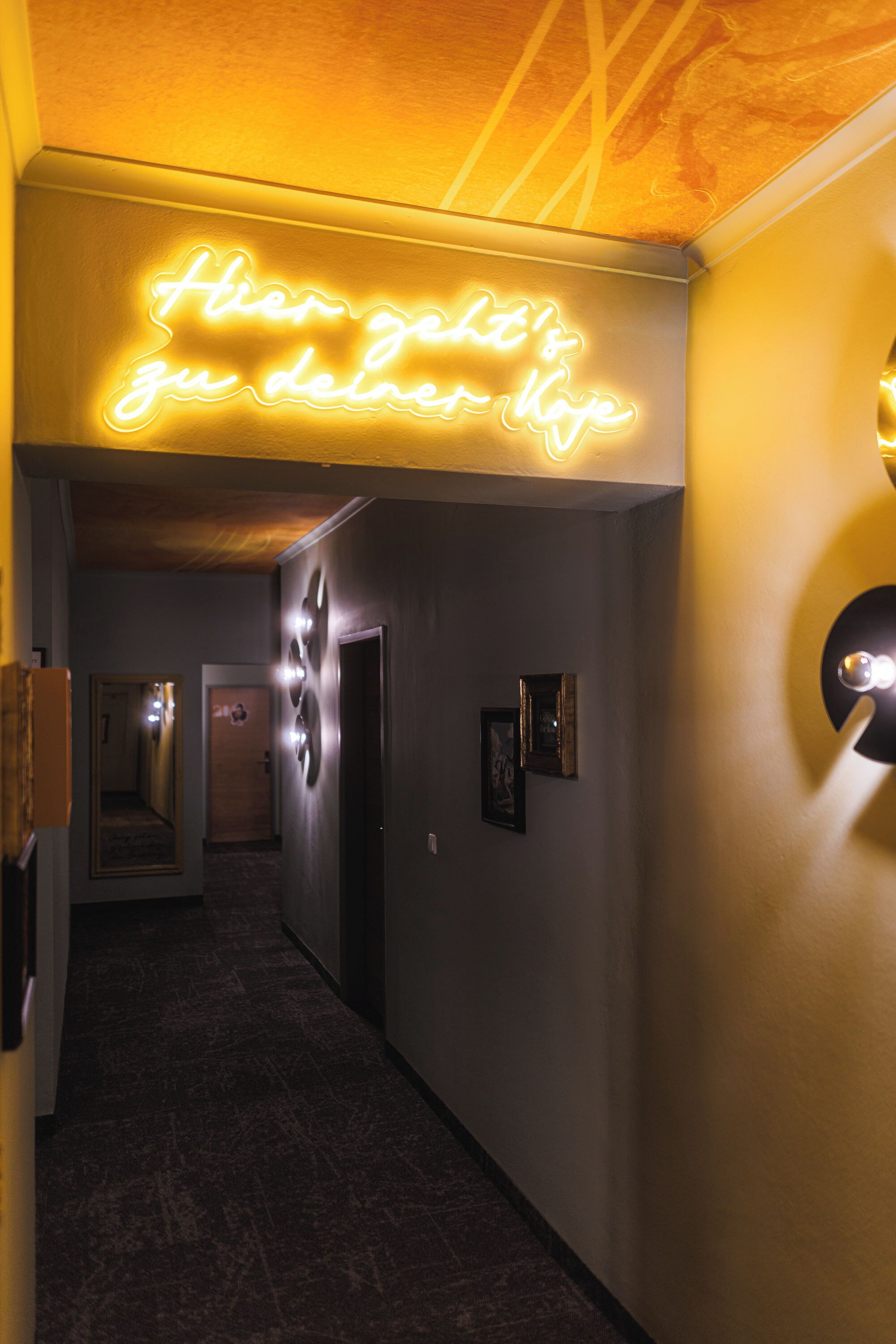 A hallway with a neon sign that reads "Here it's your home."