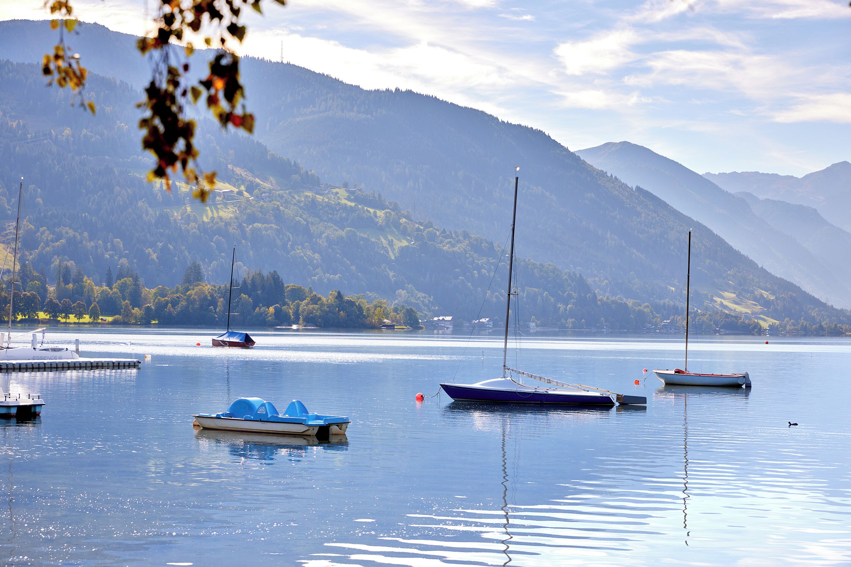 A calm lake with several boats anchored, surrounded by mountains and clear skies.