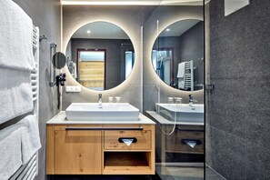 A modern bathroom with a wooden vanity, two sinks, a mirror, and a glass shower enclosure. - Fish'Inn Zell - Hotel Fischerwirt (Zell am See)