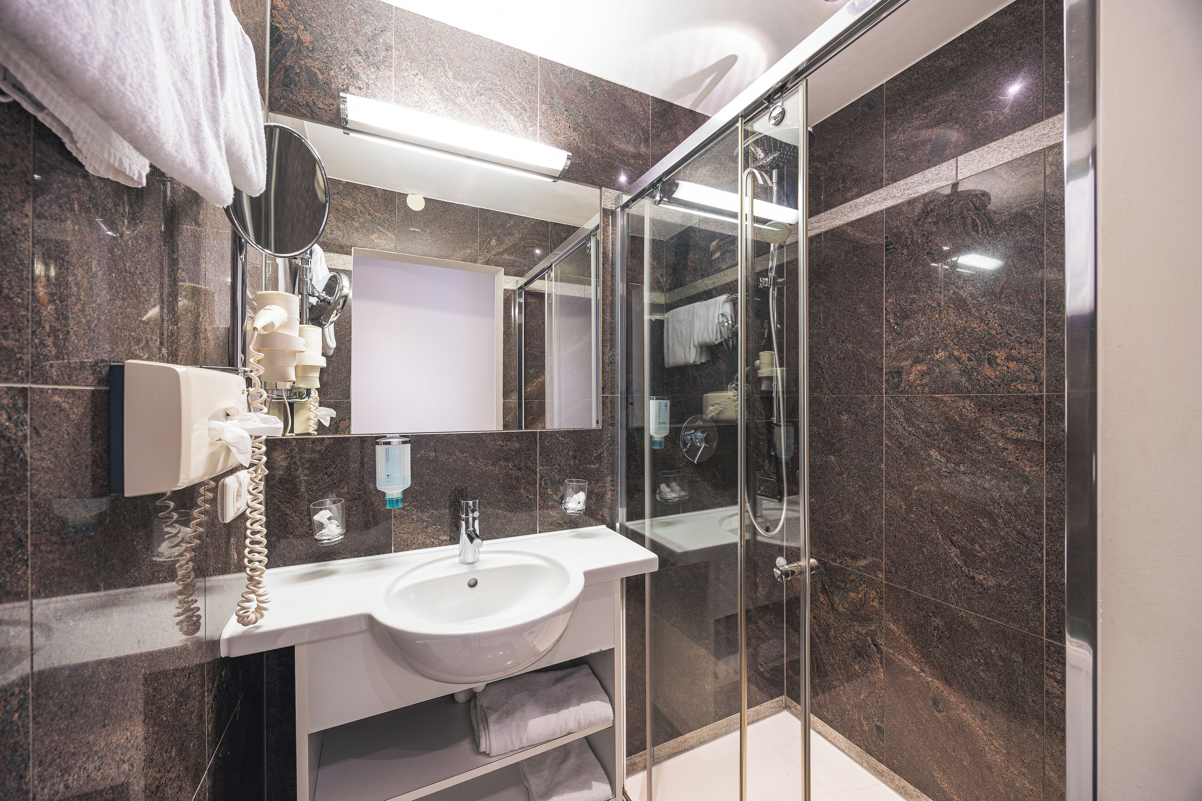 A modern bathroom with a glass-enclosed shower, a white sink, and a marble-tiled wall.