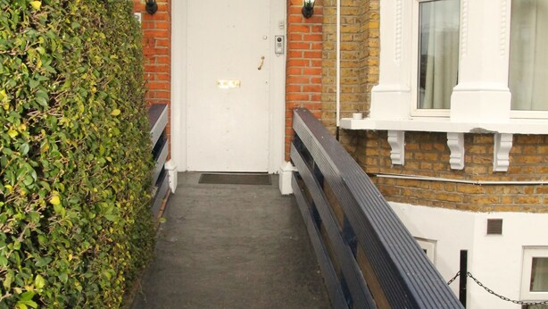 Un étroit sentier bordé de murs de briques menant à une porte blanche avec une plaque portant un numéro.
