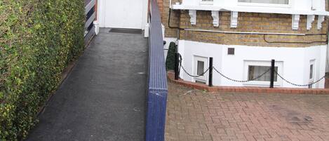 A narrow pathway leading to a white front door of a terraced house with brick walls and white trim.