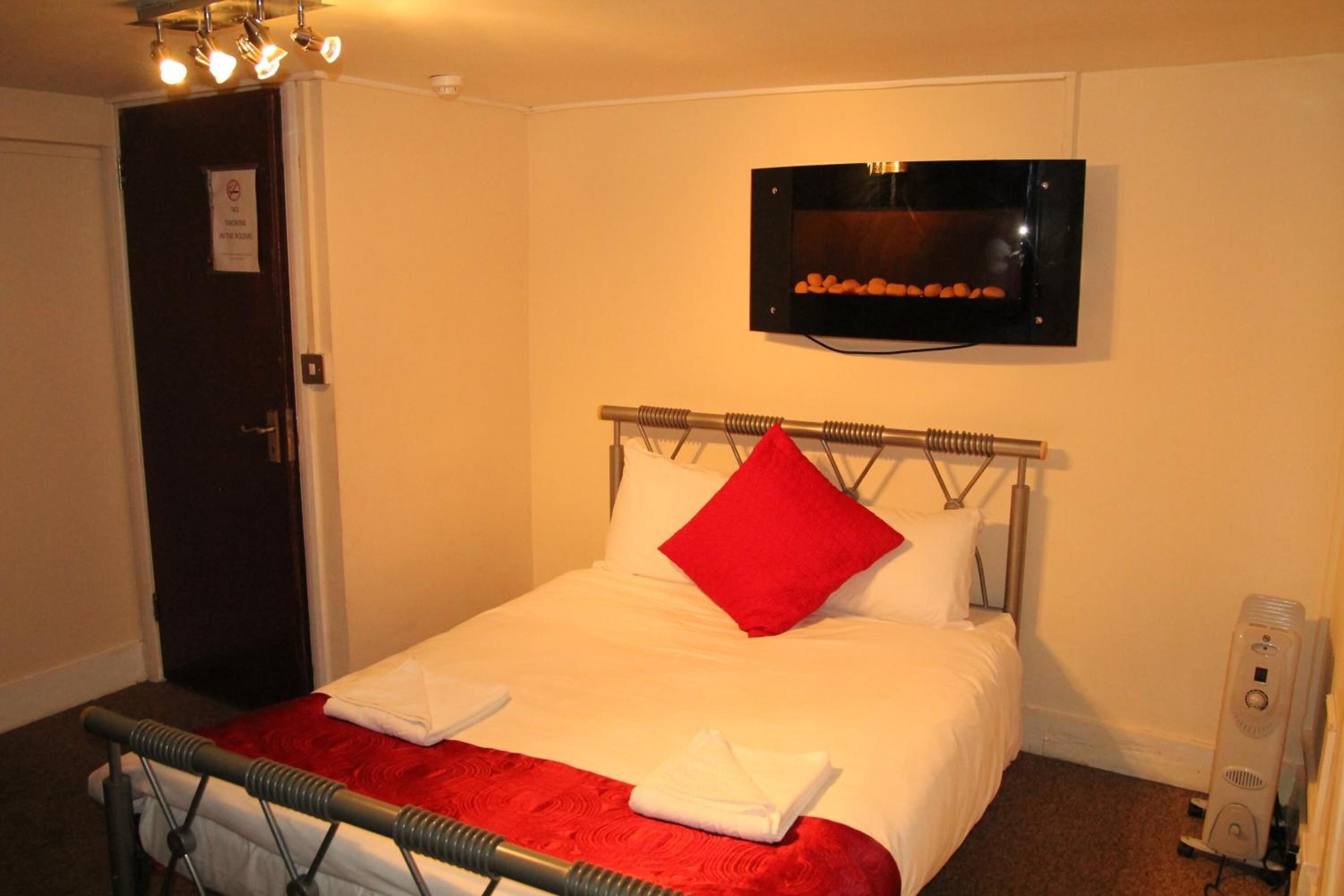 A hotel room with a bed, a TV mounted on the wall, a heater, and a door with a sign.