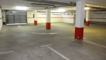 Un estacionamiento interior con pisos de concreto, pilares rojos y blancos, y flechas direccionales en el suelo.