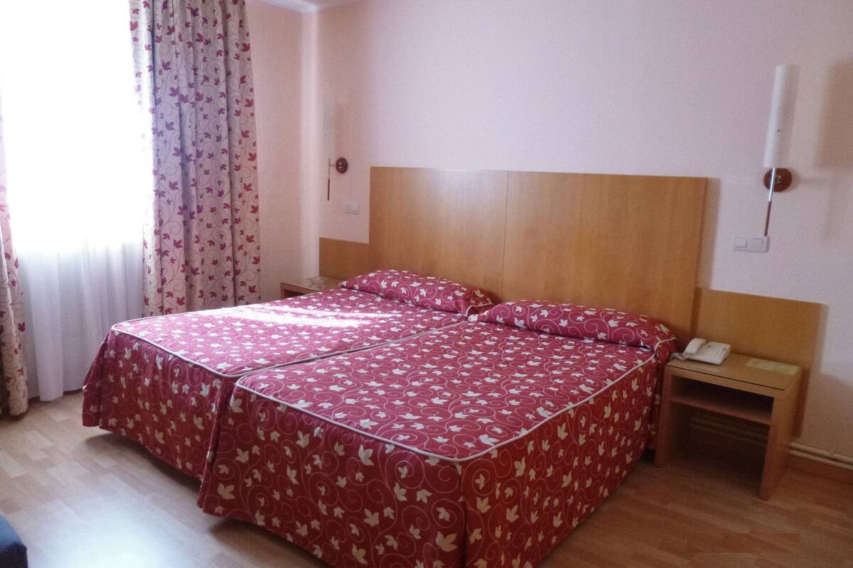 A hotel room with a bed, a nightstand, a telephone, and a window with curtains.