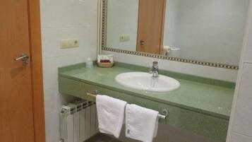 Un baño con encimera verde, lavabo blanco y espejo encima. Se ve un perchero con dos toallas blancas colgadas y un radiador debajo.