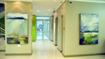 A hallway with abstract paintings on the walls, a staircase to the left, and a door at the end.
