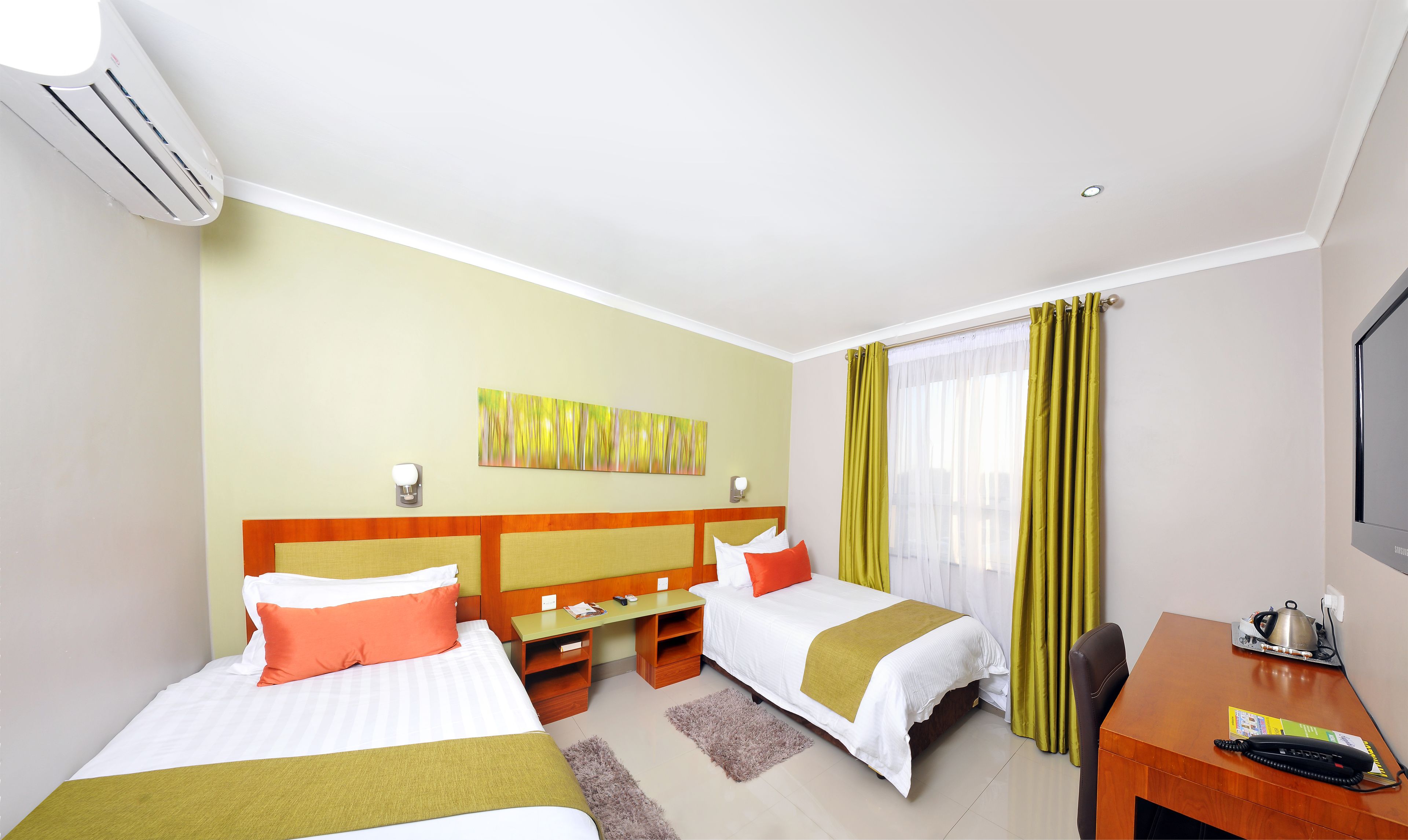 A hotel room with two beds, a desk, a chair, a television, and an air conditioning unit.