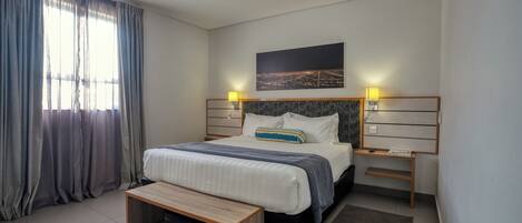 Un dormitorio moderno con una cama, un banco, mesitas de noche y un cuadro de un paisaje urbano.