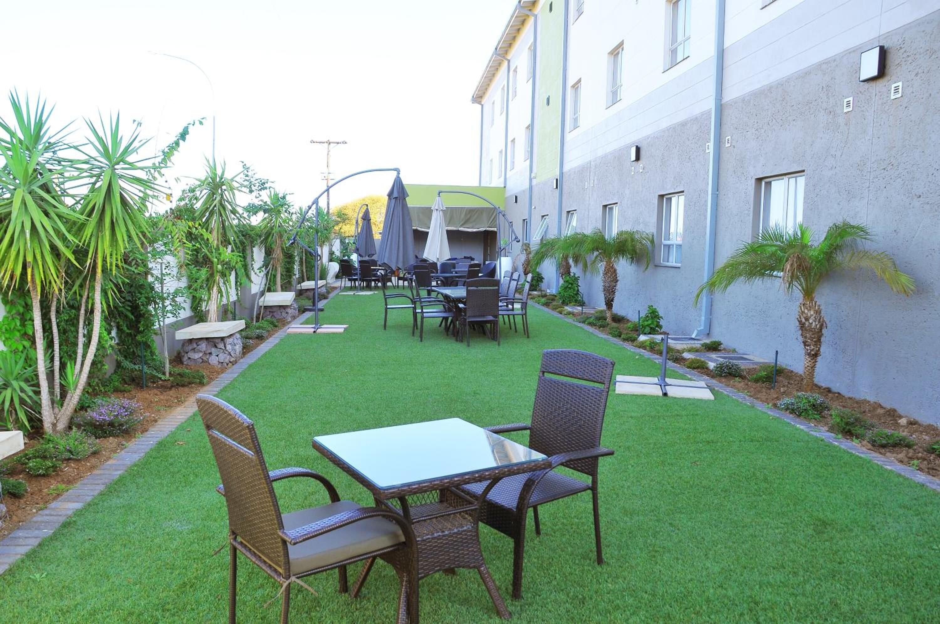 Un patio al aire libre con una mesa y sillas, rodeado de follaje y un edificio.