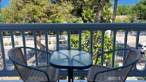 A balcony with a round table and two wicker chairs, overlooking a coastal area with trees and a view of the sea. - Theodorou Beach (Kos)