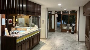 A hotel lobby with a marble floor, a reception desk with a glass partition, and wooden paneling on the walls. - Theodorou Beach (Kos)
