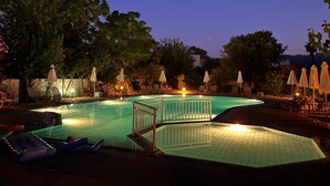 A swimming pool with lounge chairs and umbrellas, surrounded by trees and a fence. - Theodorou Beach (Kos)