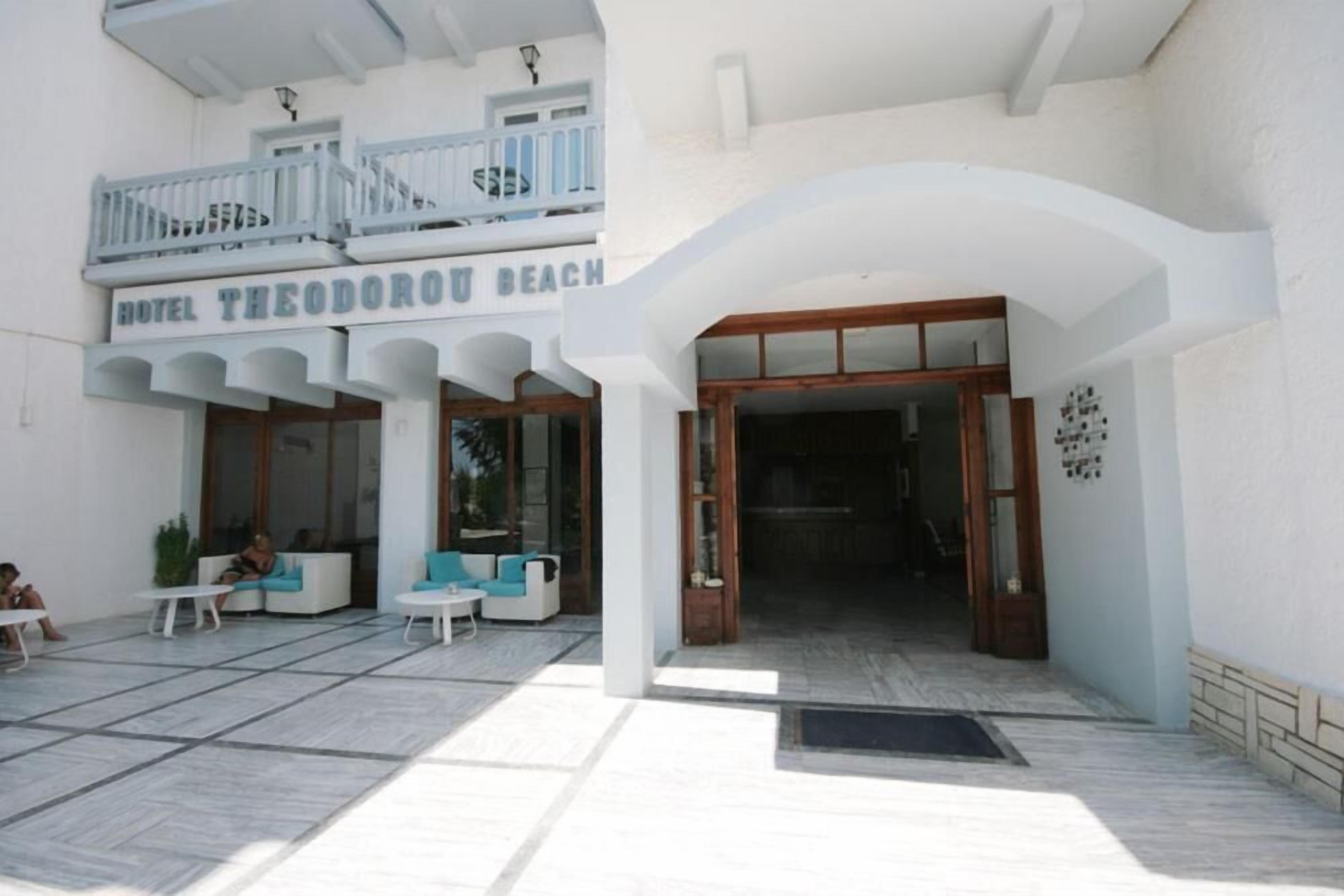 The entrance of Hotel Theodorou Beach with a covered outdoor seating area and a balcony.