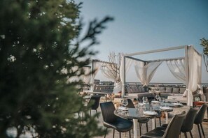 An outdoor dining area with tables and chairs, a covered seating area, and a view of the cityscape.