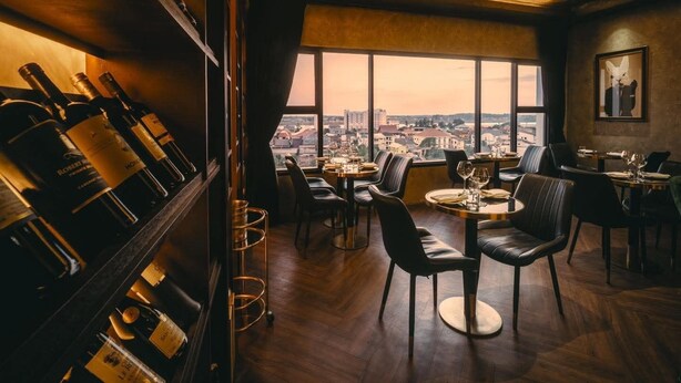 Un restaurante con vistas a un paisaje urbano, suelos de madera y una estantería con botellas de vino.