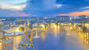 Terraza en la azotea con mobiliario exterior y vista a la ciudad al atardecer.