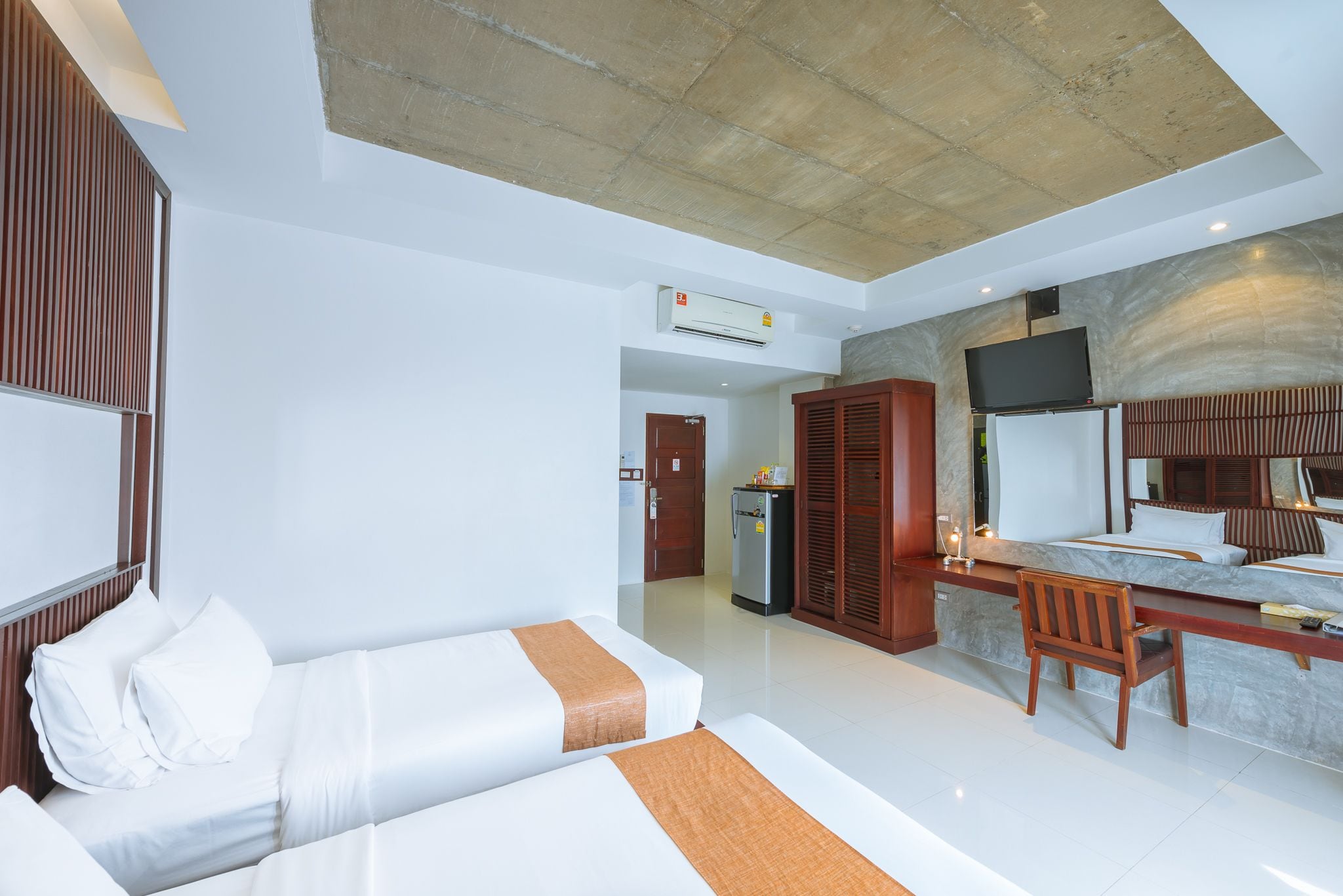 A hotel room with a bed, a desk, a chair, a television, and an air conditioning unit.