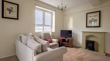 A living room with a beige sofa, a television on a wooden stand, a fireplace, and framed pictures on the walls.
