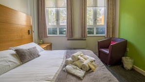 Habitación de hotel con cama, una silla, ventana con cortinas y vistas al exterior.