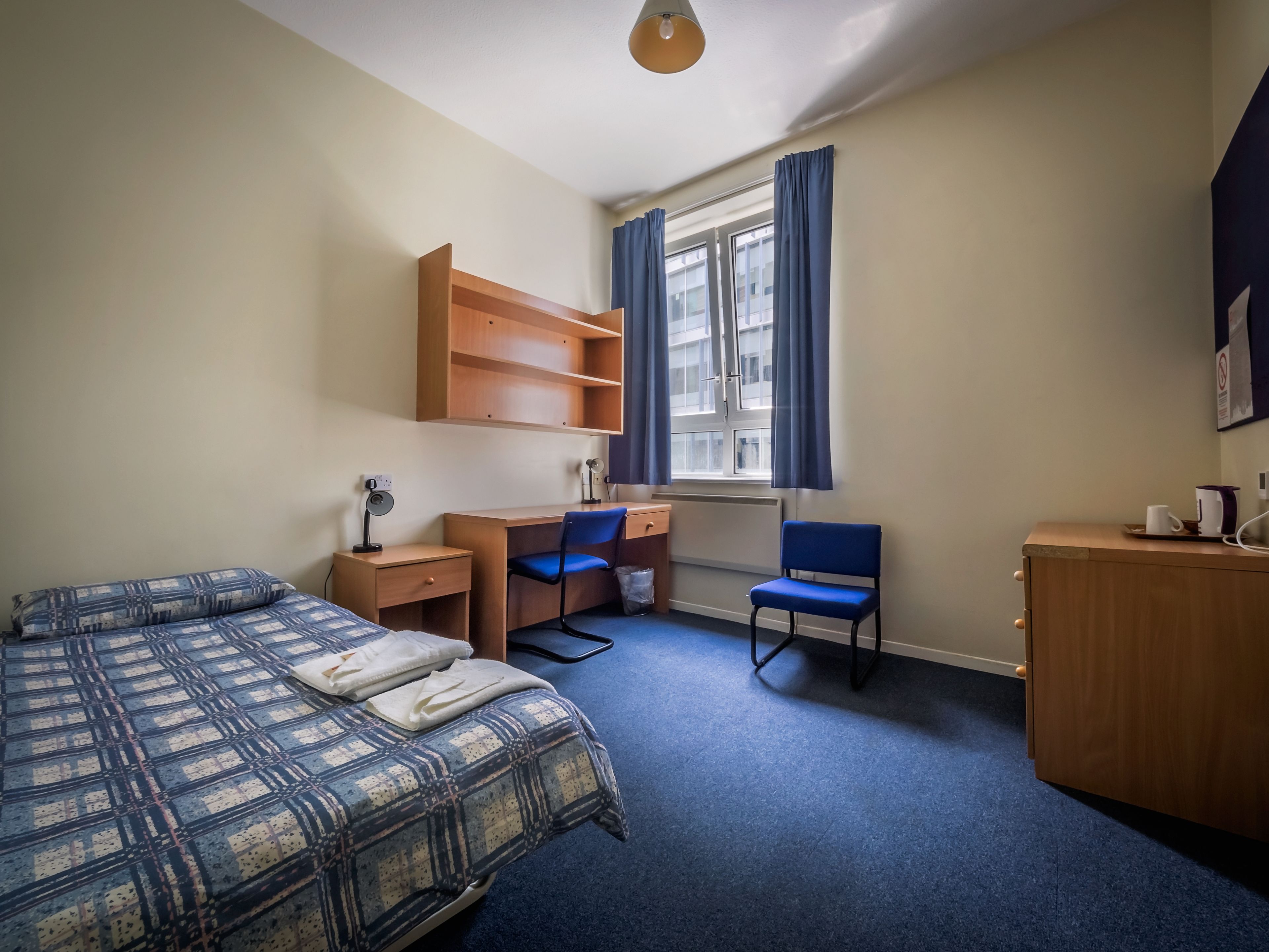 A bedroom with a bed, desk, chair, and wardrobe.