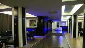 Un moderno vestíbulo de hotel con un mostrador de recepción alargado, una zona de comedor con sillas y un cuadro grande en la pared.