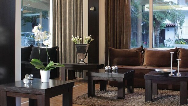 Una sala de estar moderna con un sofá marrón oscuro, una mesa de centro y un televisor. Hay plantas en macetas y vistas de vegetación al exterior.