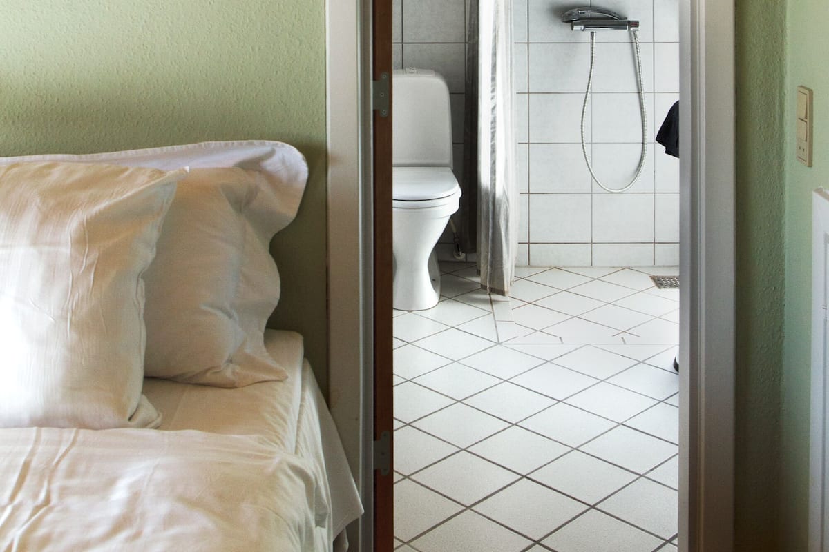 A bathroom with a shower, toilet, and a bed with white bedding.
