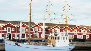 En stor, lyseblå båd ved navn OKE ligger ved et havneanlæg med røde bygninger i baggrunden.