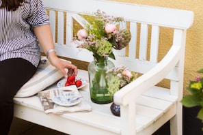 A white bench with a vase of flowers and strawberries on a table.