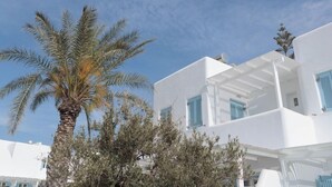 Un edificio bianco con persiane blu, circondato da alberi e un cielo sereno.