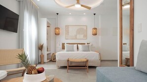Una camera d'albergo moderna con un letto, una scrivania con una ciotola di frutta, una sedia, un tavolino e una ventola a soffitto.