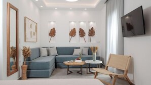 Un soggiorno moderno con un divano blu, un tavolino rotondo, una poltrona in vimini e decorazioni a tema foglie sulla parete.