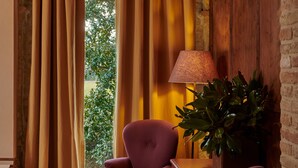 Una habitación con techo de madera, un ventanal con cortinas, una lámpara y dos sillas.